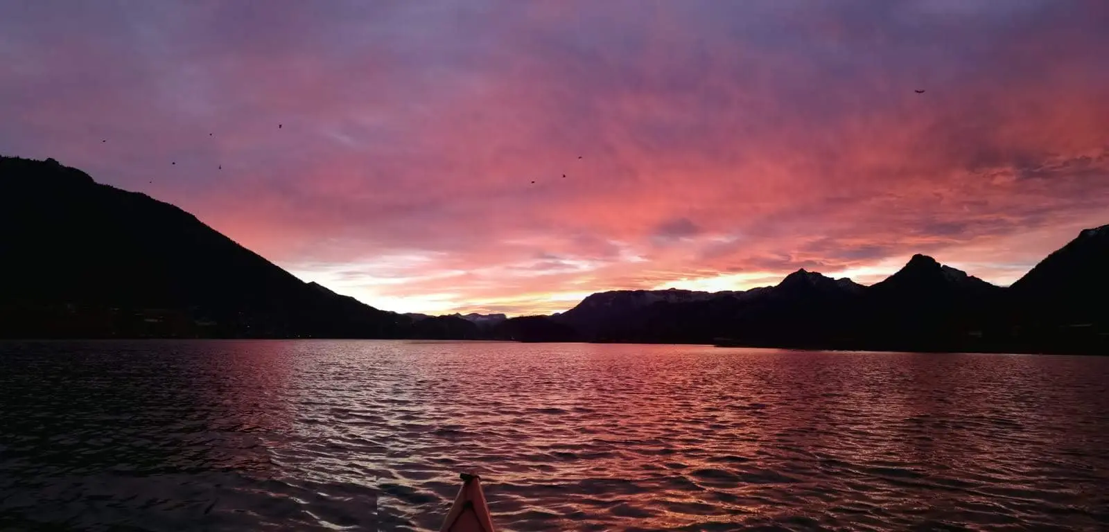 Sonnenuntergang über dem Wasser, Blick vom Bug eines Kanus auf die Berge